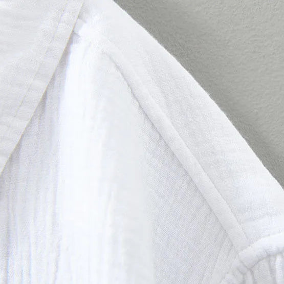 Zoom sur le tissu de la chemise blanche pour homme. Tissu en double gaze froissée de qualité, doux au toucher, avec une finition texturée légèrement froissée pour une allure élégante et décontractée. La matière permet une grande respirabilité et confort tout au long de la journée.