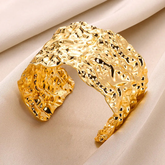 Bracelet manchette doré en acier inoxydable sur fond blanc, bijou pour femme à la forme irrégulière et look vintage.