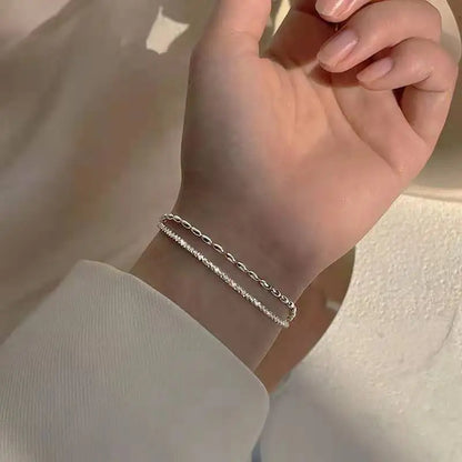 Poignet d’une femme habillée de façon chic, avec le bracelet en argent superposé à d’autres bijoux fins.