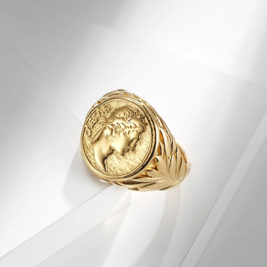 Chevalière en métal doré avec motif de pièce antique, style old money chic.