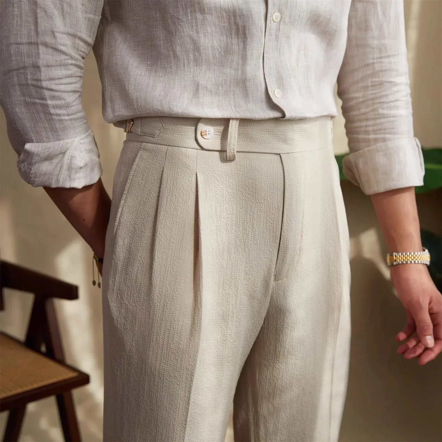 Pantalon ASHBURY beige, vue de demi-profil. Ceinture boutonnée et ajusteurs latéraux pour un maintien sur mesure. Alliance parfaite entre modernité et héritage tailleur.